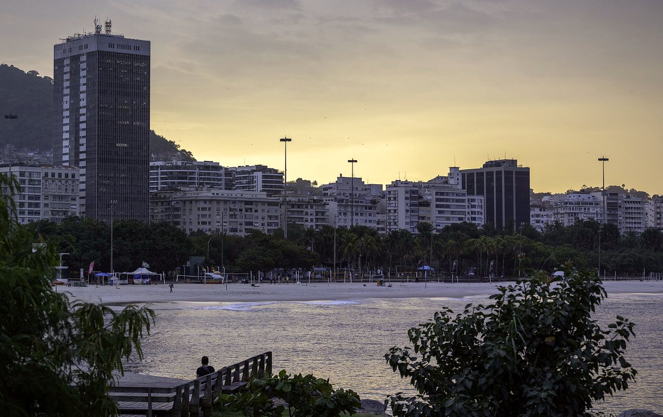 Apartment buildings along Botafogo beach at dusk, with palm trees and the calm water of Guanabara Bay