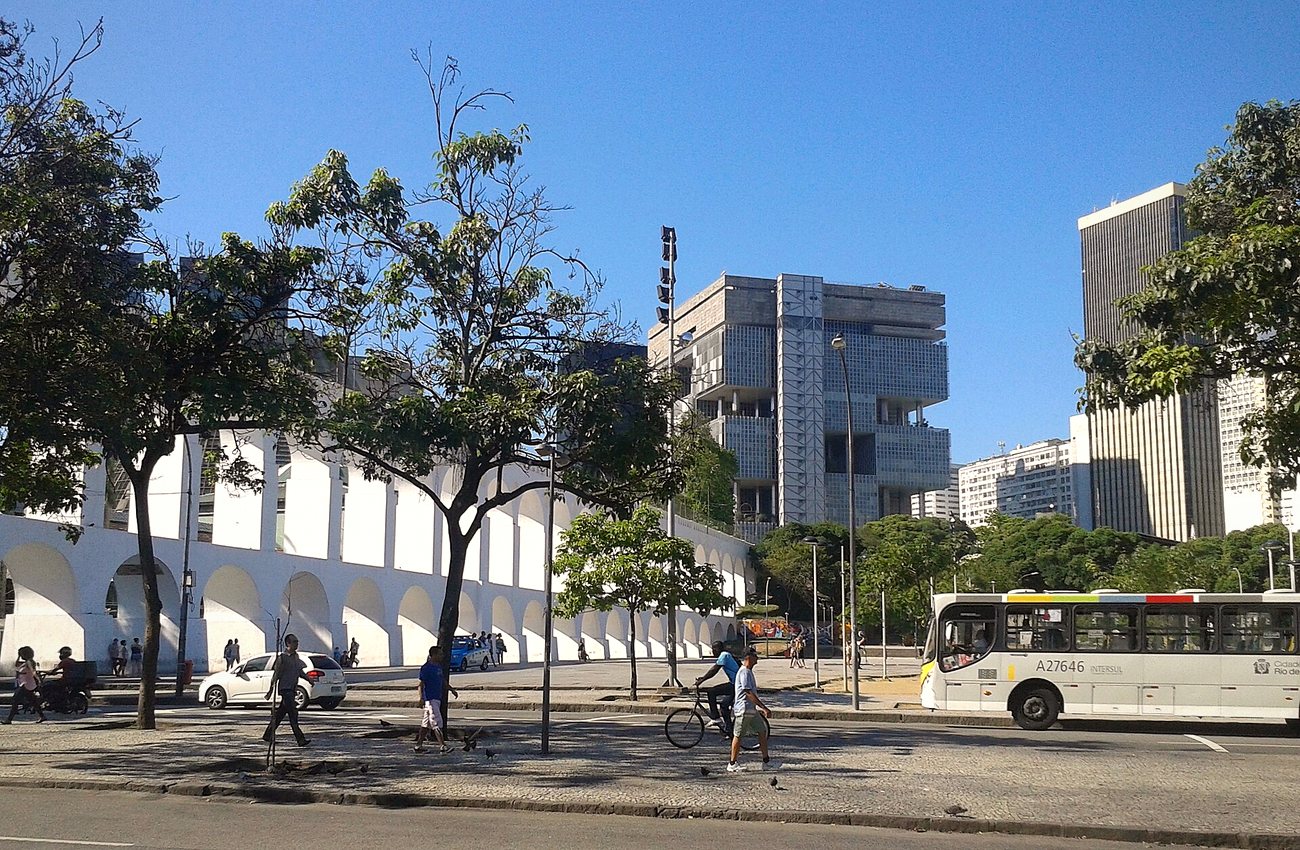 The white arches of the Lapa Aqueduct in central Rio de Janeiro with office towers behind and a city bus on the avenue